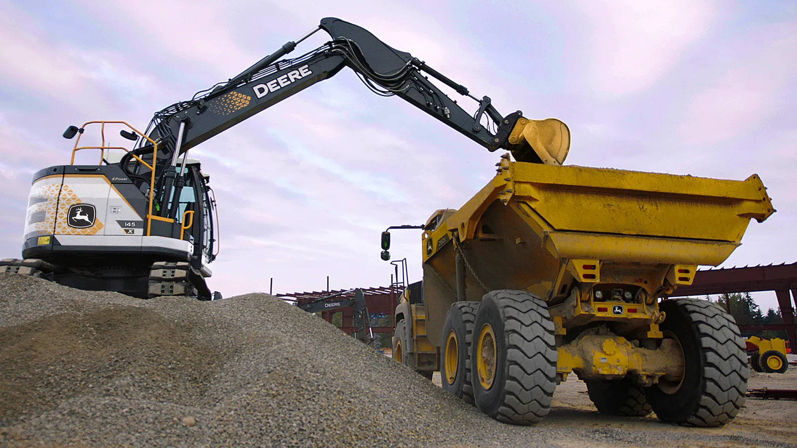 John Deere heavy equipment loads dirt into a dump truck.