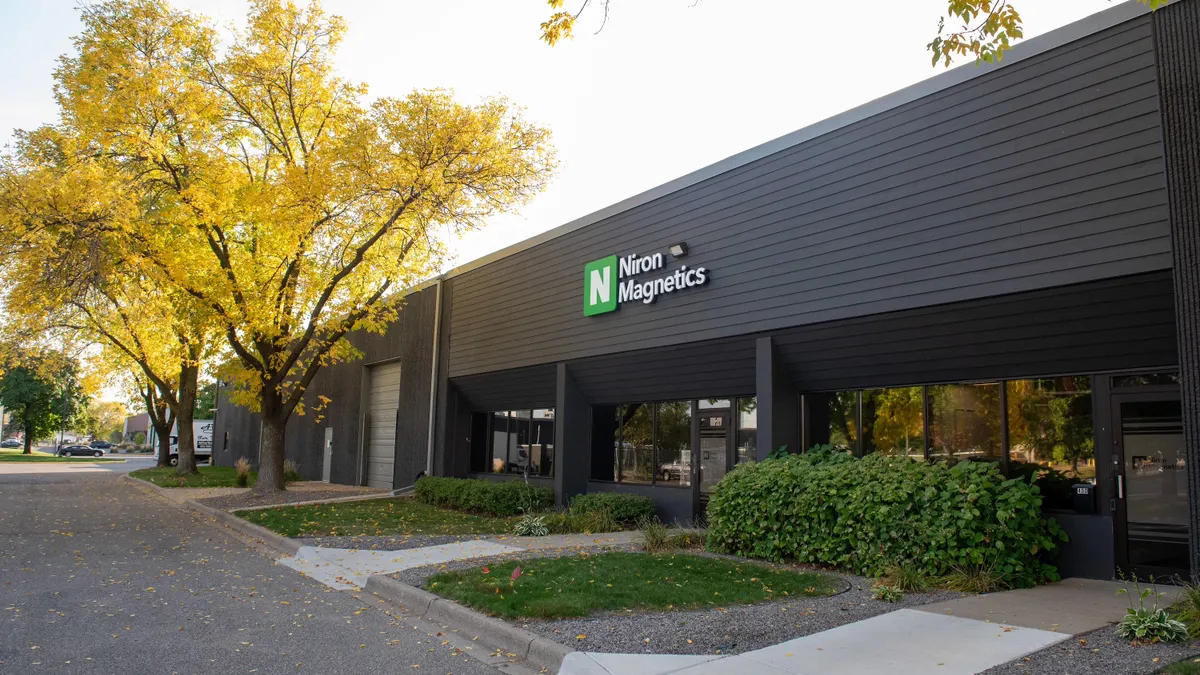 The exterior of dark brown building with a white and green Niron Magnetics sign above glass doors.