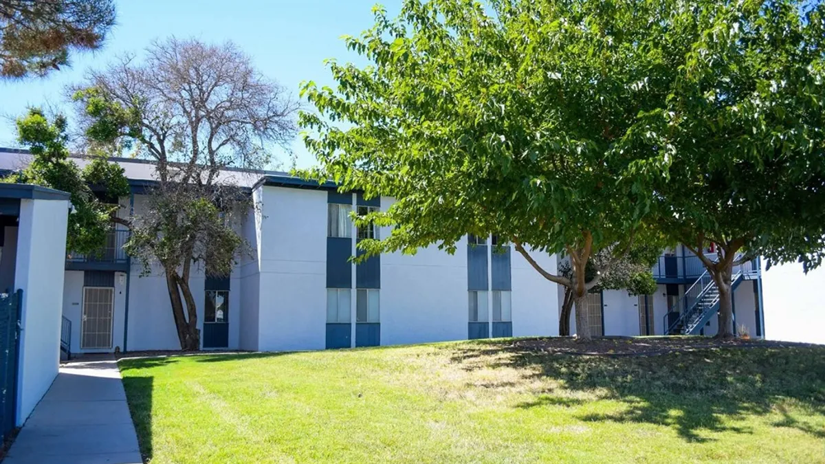 White, two-story apartments with tree and grass in the foreground