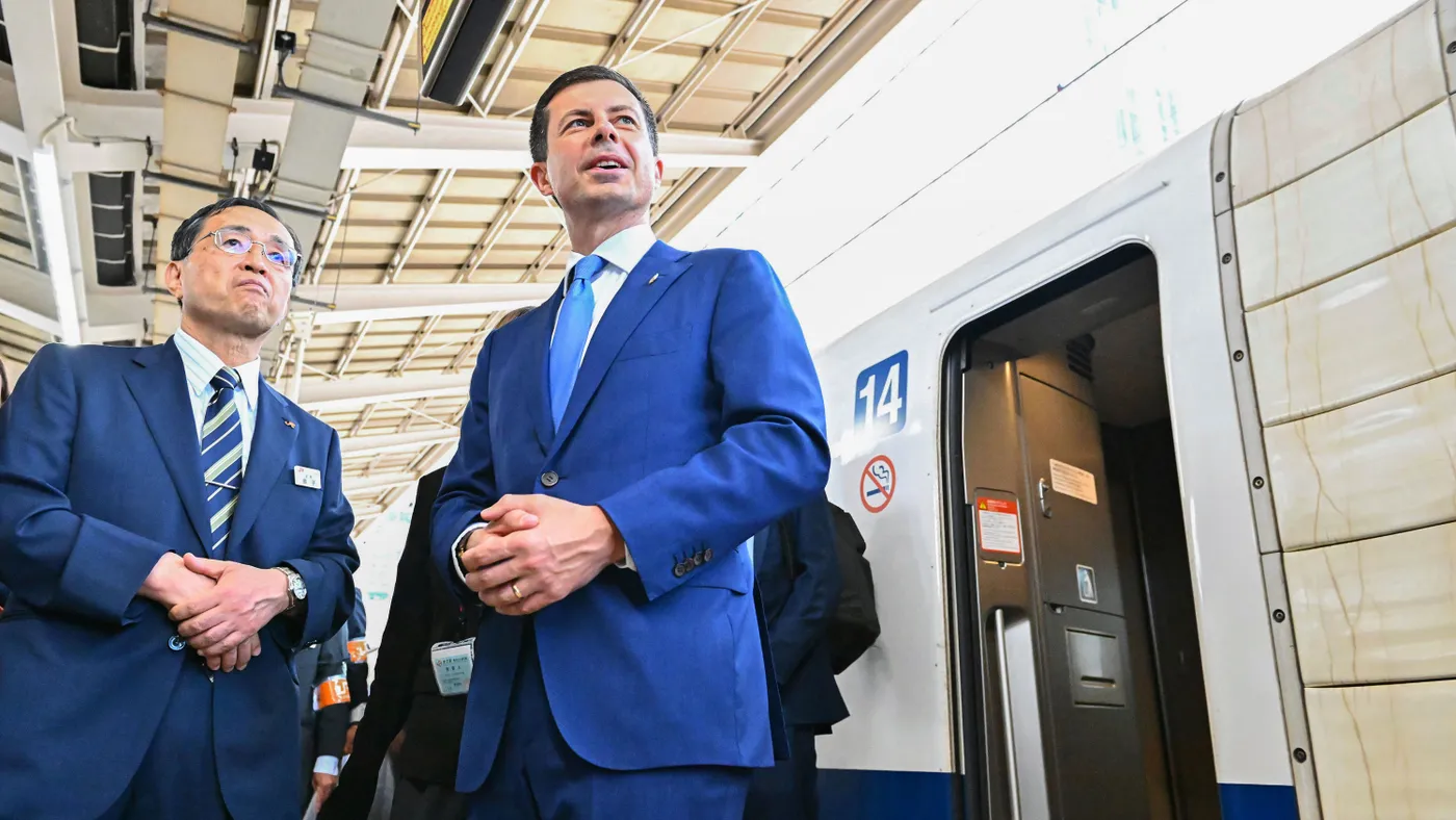 Two men in suits standing in front of a high-speed train at a station.