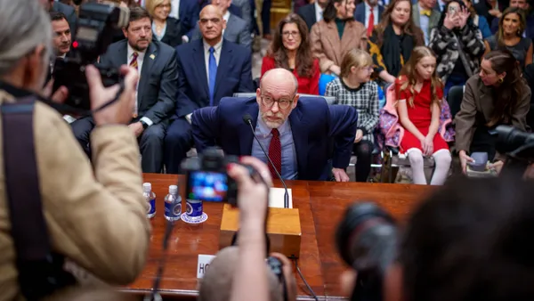 A man sits at a table as photographers stand over him.