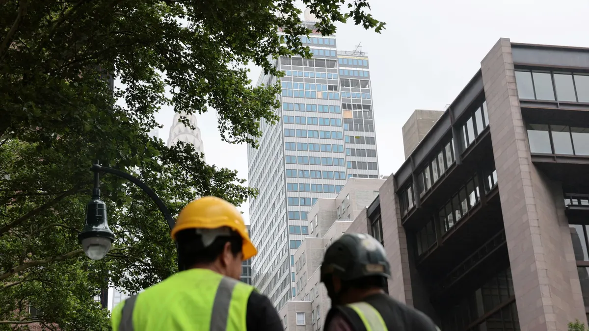 Two construction workers look up at a tall building.