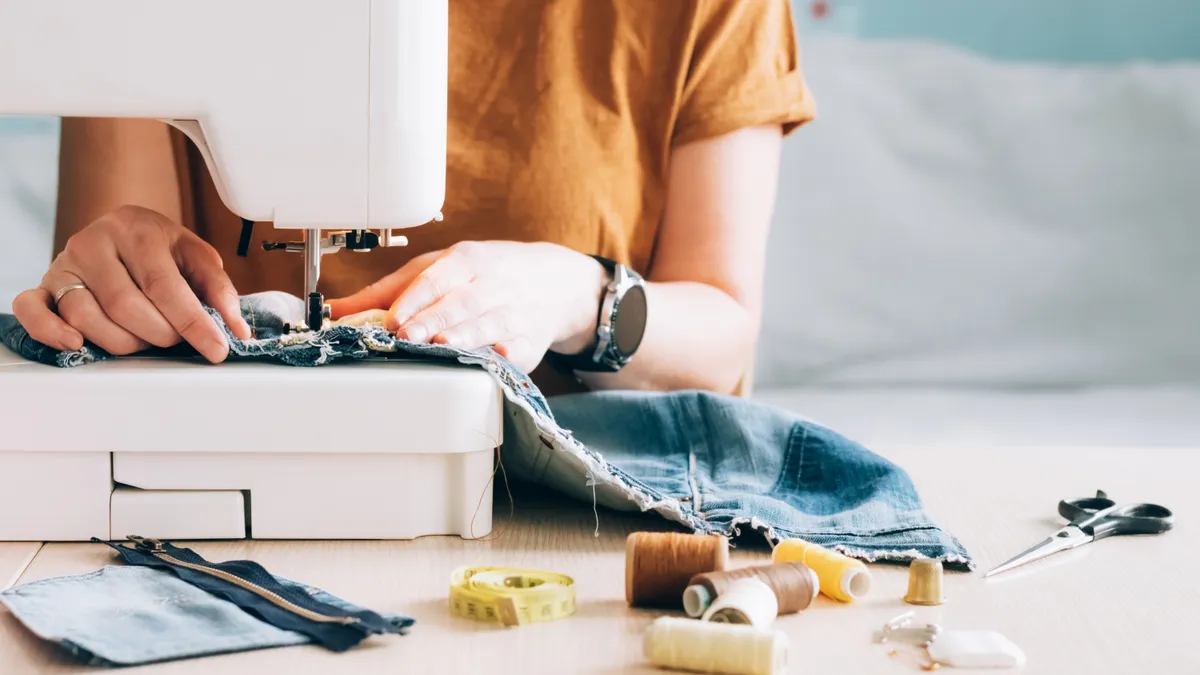 A tailor works at a sewing machine, reusing fabric from old denim clothes.