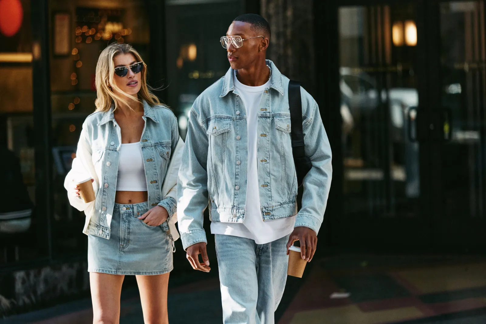 Two people cross the street in denim jackets and bottoms.