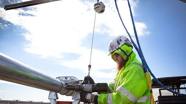 A man puts a claw-shaped tool around a pipe while working in a solar field.