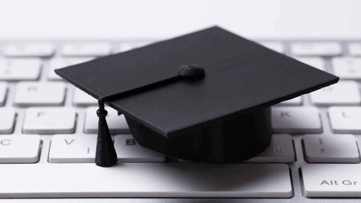 A small, black graduation cap sits on a computer keyboard