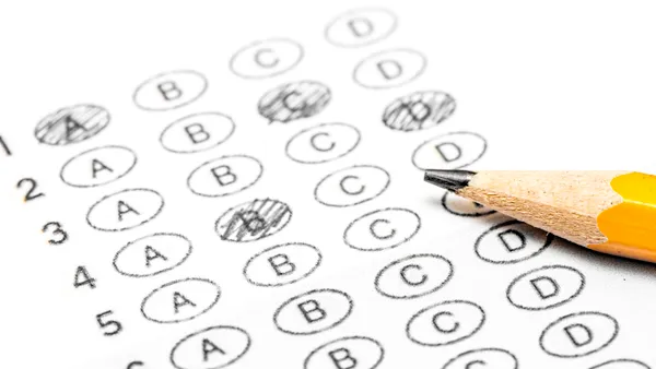 a white sheet of paper shows lines of bubbled letters to mark answers for a test. A yellow pencil rests on the paper.