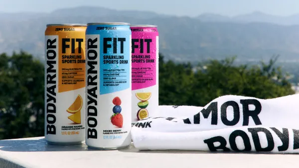 Three cans of Bodyarmor fit are pictured outdoors next to a towel.