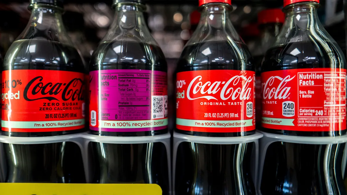 Plastic Coca-Cola bottles lined up inside a refrigerated case