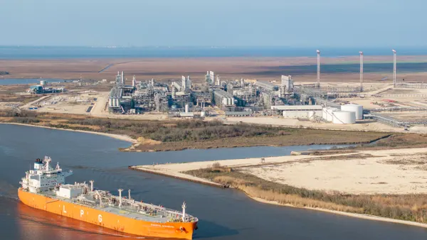 A ship cruises up a riven near a large industrial facility.