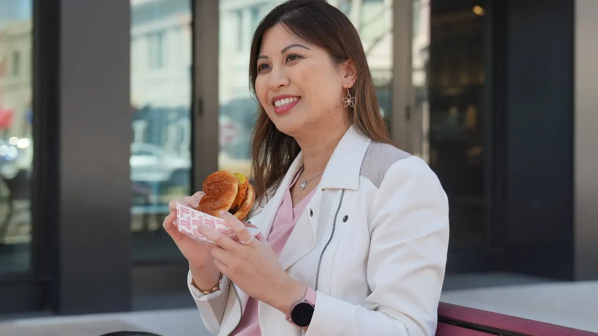 A photo of a person walking in front of a store holding a chicken sandwich.