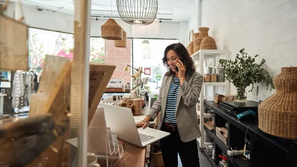 A person on their phone and looking at their laptop in a small retail store