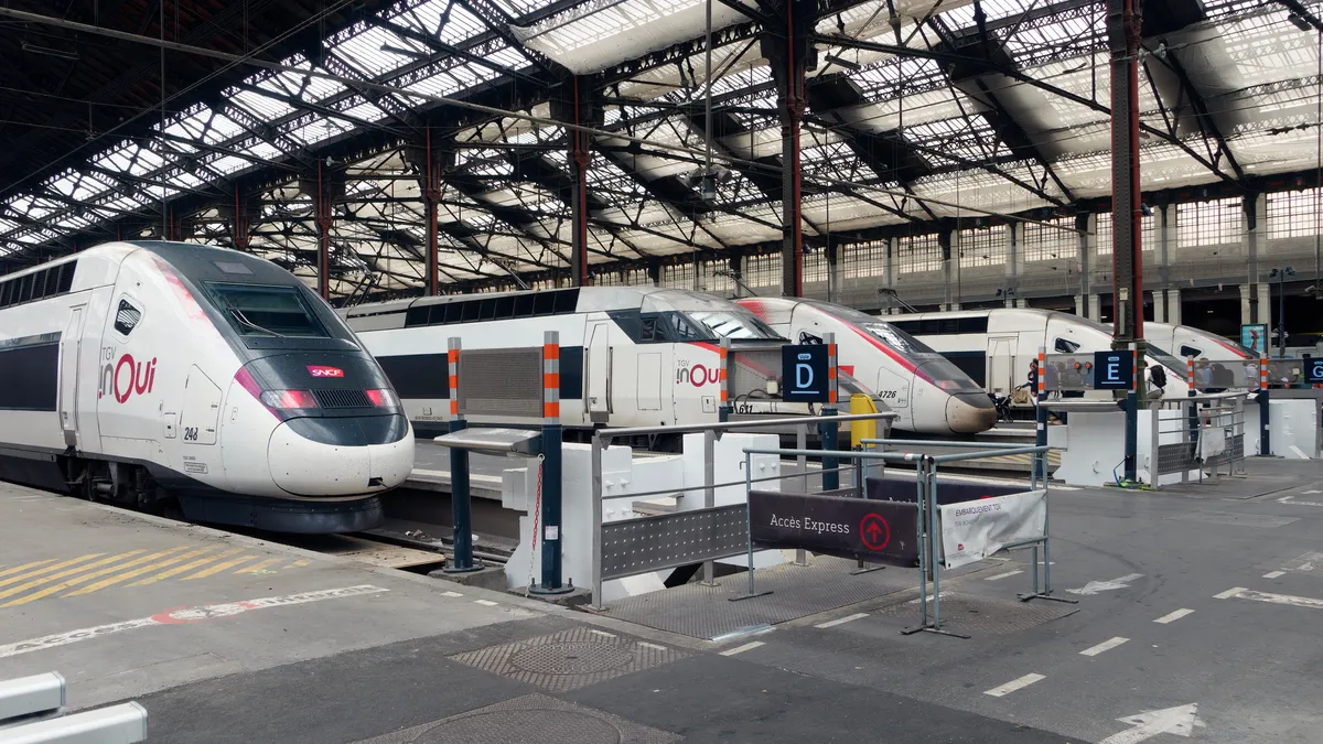 Five white TGV high-speed trains are lined up at a large train station in Paris.