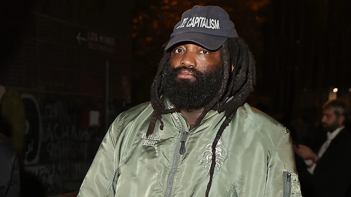 A person in a ballcap and green jacket walks toward the camera.