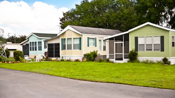 A row of three small homes with a grass lawn and trees in the background.
