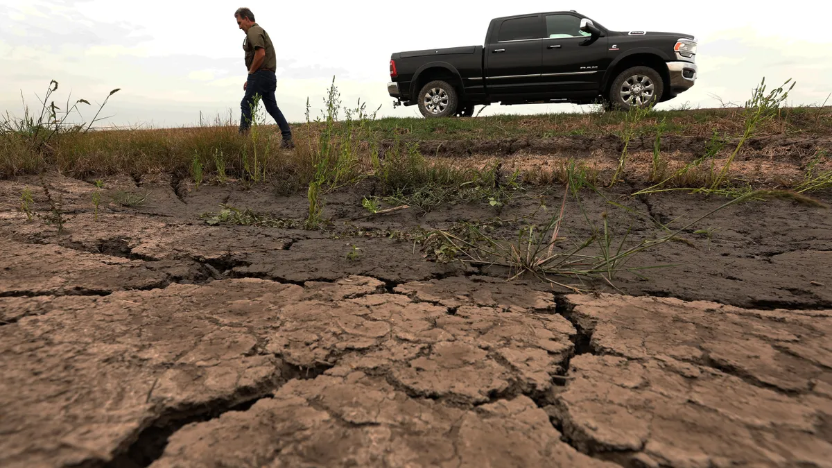 Cracked earth is seen as a farmer stands near his truck in the distance.