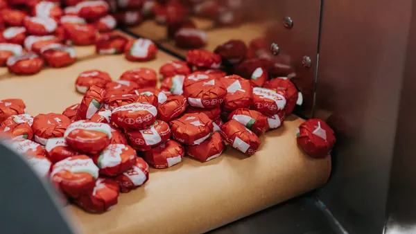 Dozens of Babybel cheese products in red packaging come off a production conveyor belt.