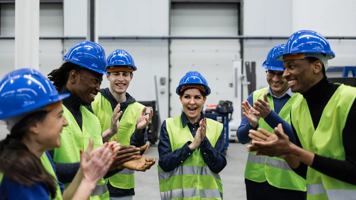 A group of racially diverse workers gather in a robotic factory.