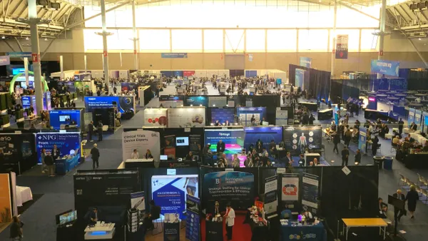 An overhead shot of a conference hall shows many booths with people gathering.