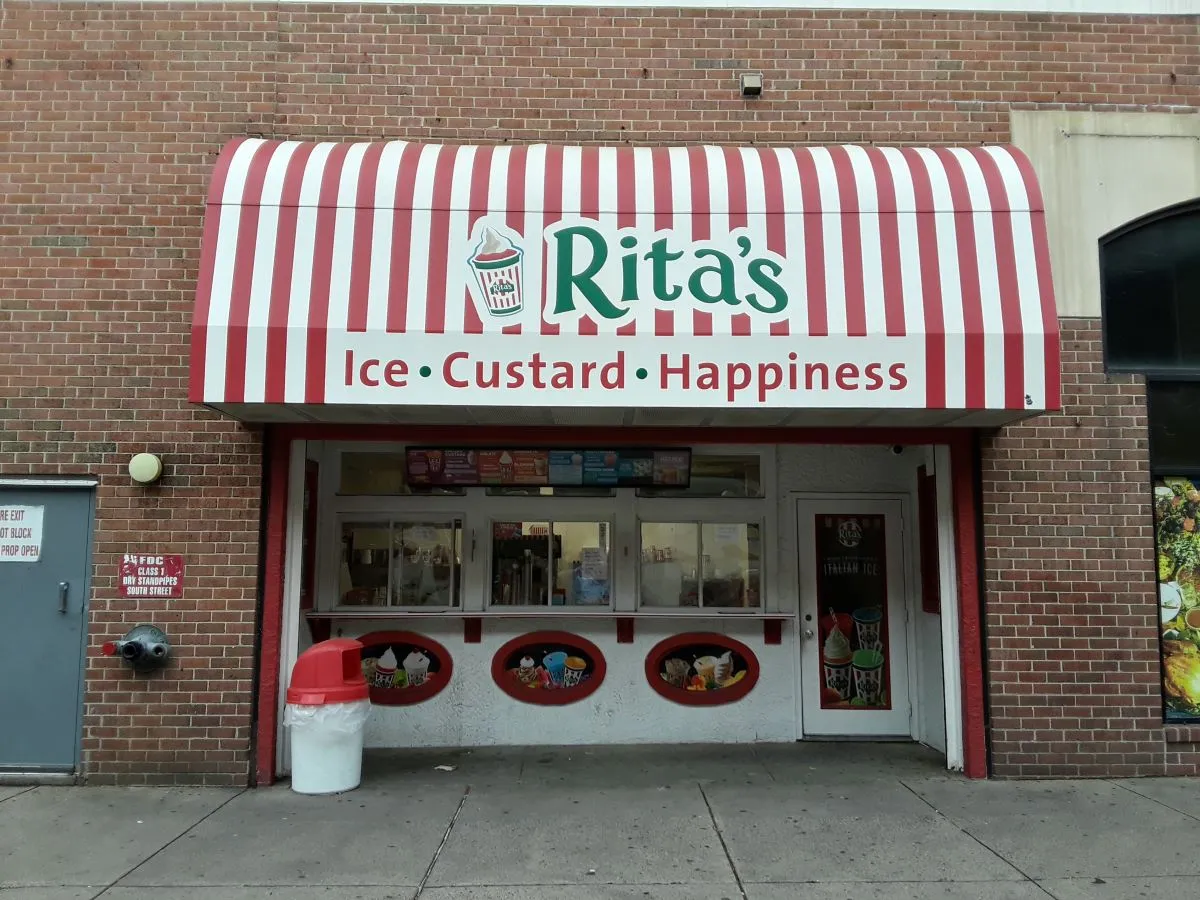 An image of a brick building with a red and white striped sign that says "Rita's Ice, Custard, Happiness"