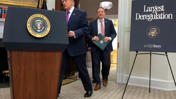 President Donald Trump walks to a podium with the presidential seal followed by EPA Administrator Lee Zeldin. A sign on the stage says "Largest Deregulation in U.S. History."