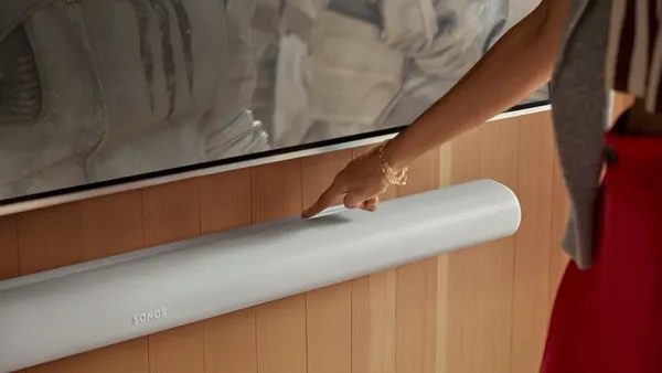 A close up of a woman's hand touching a Sonos speaker.