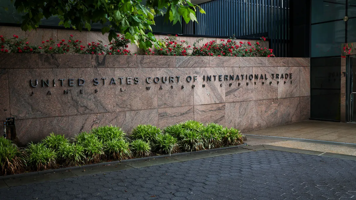 An exterior image of a wall outside the U.S. Court of International Trade. The wall has lettering that reads "United States Court of International Trade James I. Watson Courthouse."