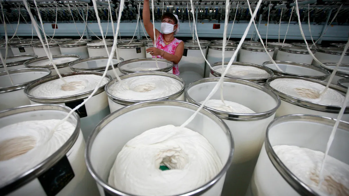 A person holds a piece of long white fiber in front of large rolls of fiber in containers.