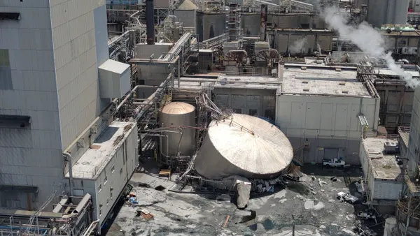 A collapsed tank amid other equipment at the exterior of an industrial site.