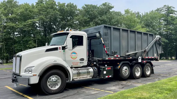A truck with a dumpster on its back and the Agri-Cycle logo on its cab is parked in a parking lot.
