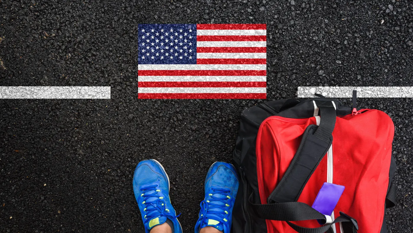Someone's sneakers stand next to a duffle bag and an American flag drawn on the pavement.