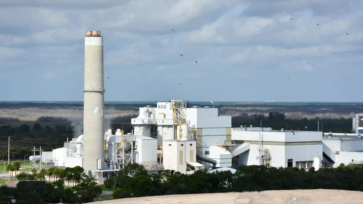 An industrial facility with a smokestack is viewed from a distance.