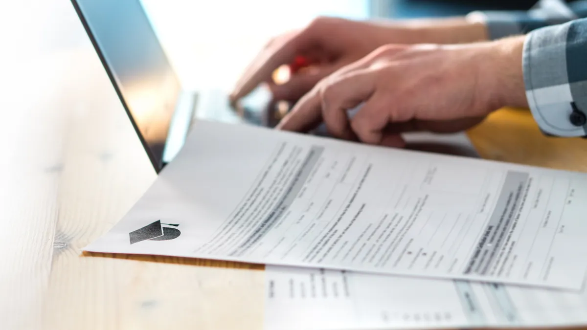 An individual writing up a college or university application form with laptop nearby.