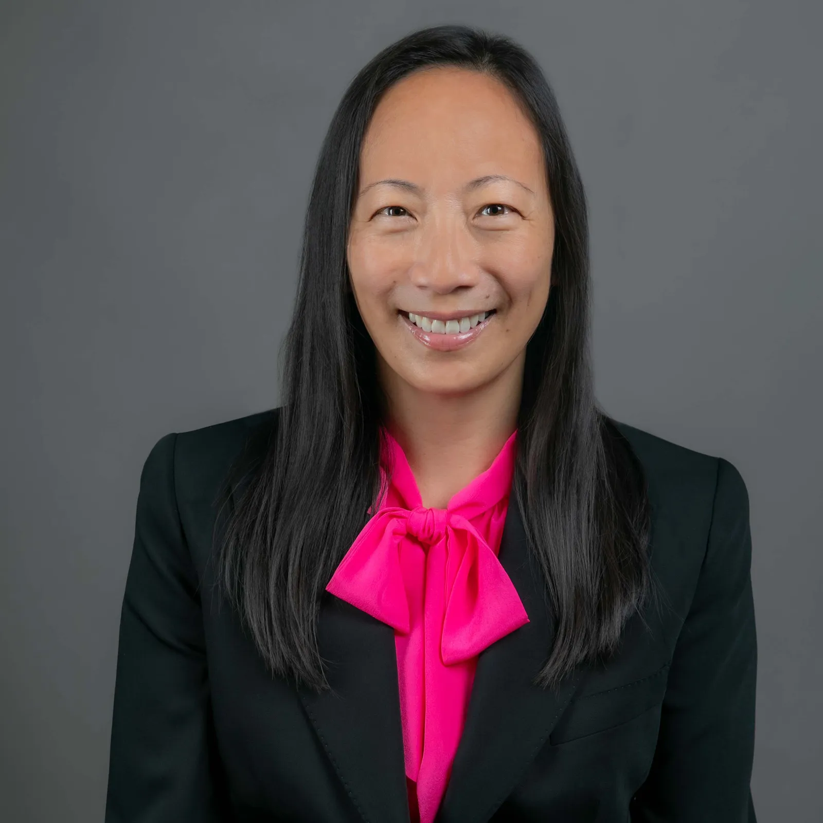 A headshot of Nadine Lee, an Asian woman with long dark hair dressed in a black suit and a pink scarf.