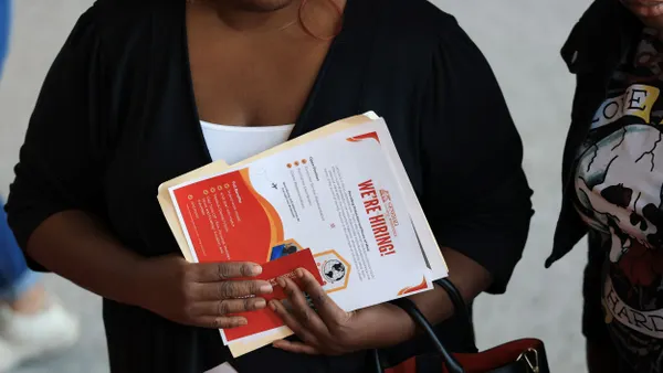 A person holds a flyer that says "We're hiring!" at a job fair.