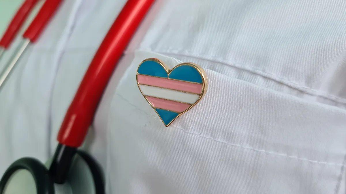 Physician in white lab coat wears a pin of the transgender flag