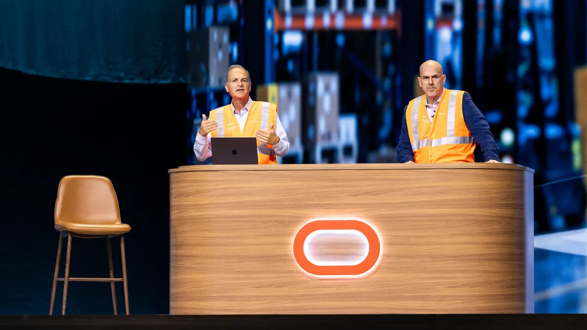 Photo of Oracle executives in safety vests demoing an agentic AI warehouse app in opening keynote at the Oracle AI World 2026 conference in Las Vegas.