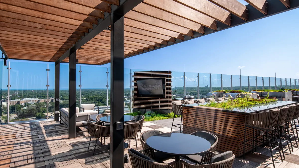 Tables and chairs among greenery on a rooftop.