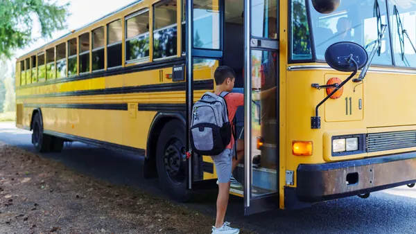 A student with a backpack gets on a yellow school bus.