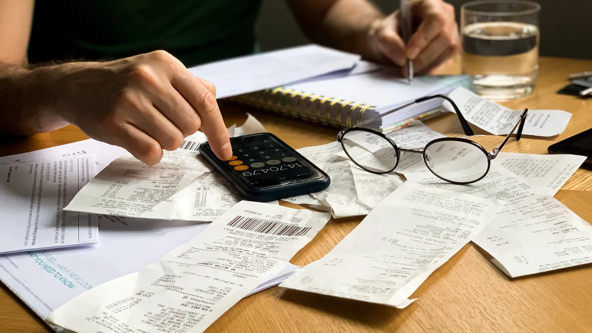 Person using calculator on phone with receipts scattered on table