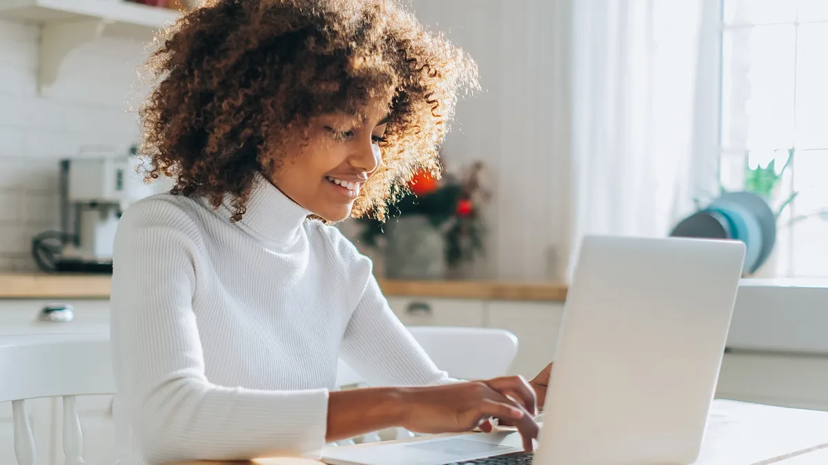 A woman with curly hair sitting at a table, focused on her laptop.