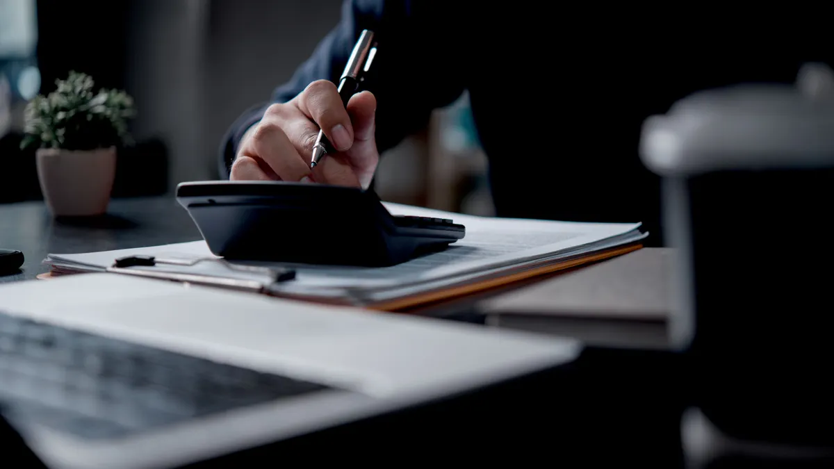 A business professional using a calculator and pen to review financial documents in an office setting.