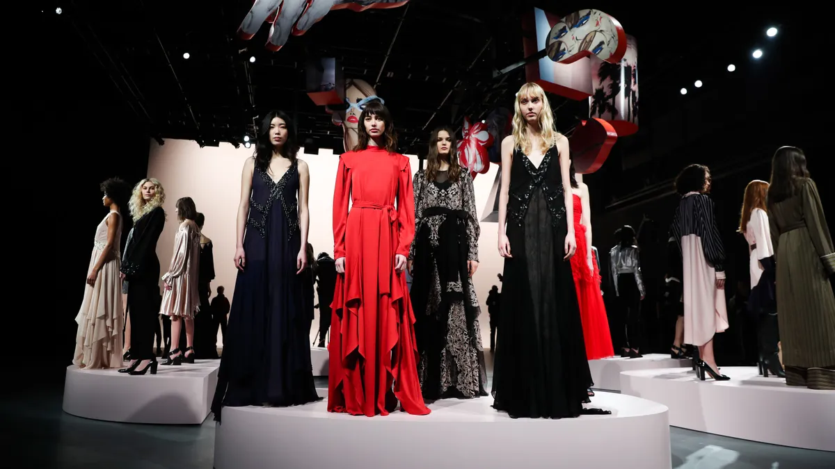 Models pose in a group wearing long dresses and standing on platforms.