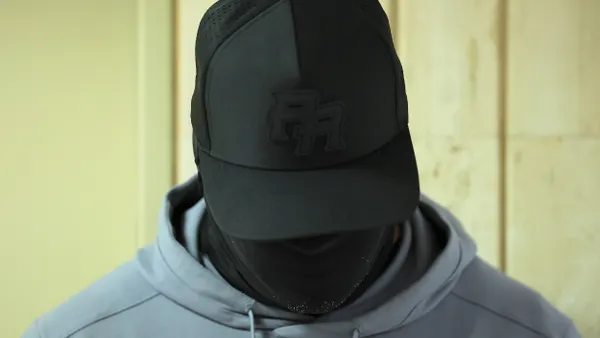 Close-up of a person's head covered with black mask, wearing black baseball hat and gray hoodie.