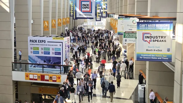 An overhead view of a convention center with banners advertising Pack Expo hanging above people walking.