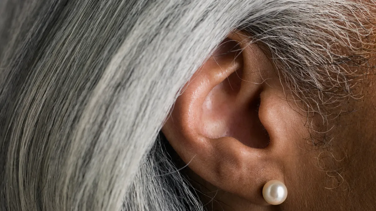 Close up of an ear: A Black femme-presenting person with straightened grey hair and a pearl earring