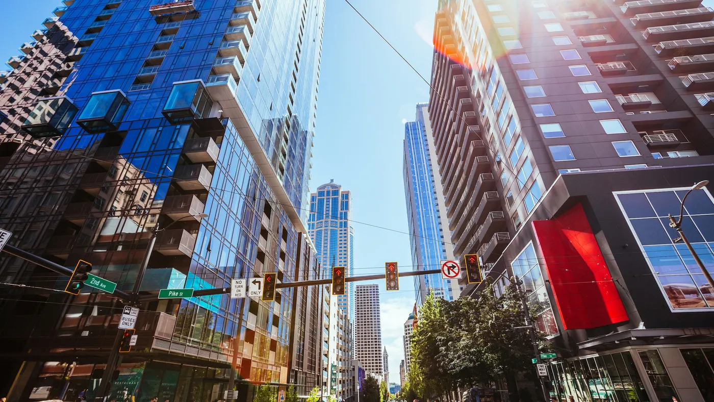 Stoplights and street between two tall buildings with more tall buildings in the background.