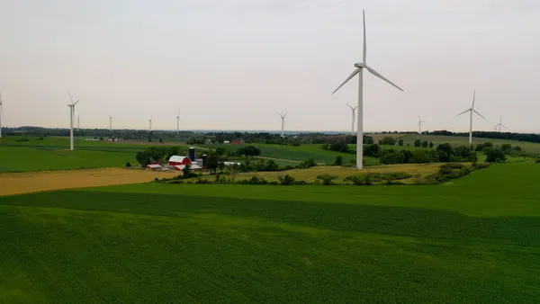 Wind turbines rise above a farm with green fields.