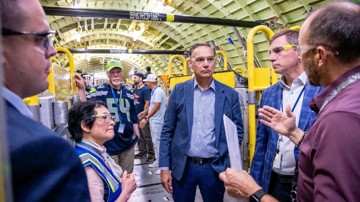 A group of people wearing protective goggles inside a plane factory.