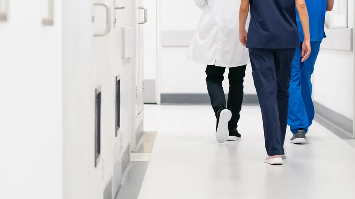 Rear view of doctor and nurse walking in hallway while discussing a case